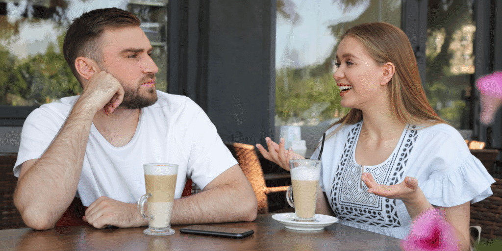 A man looks off in the distance while his date happily chats with him, illustrating someone who is disengaged and not that interested in this date.