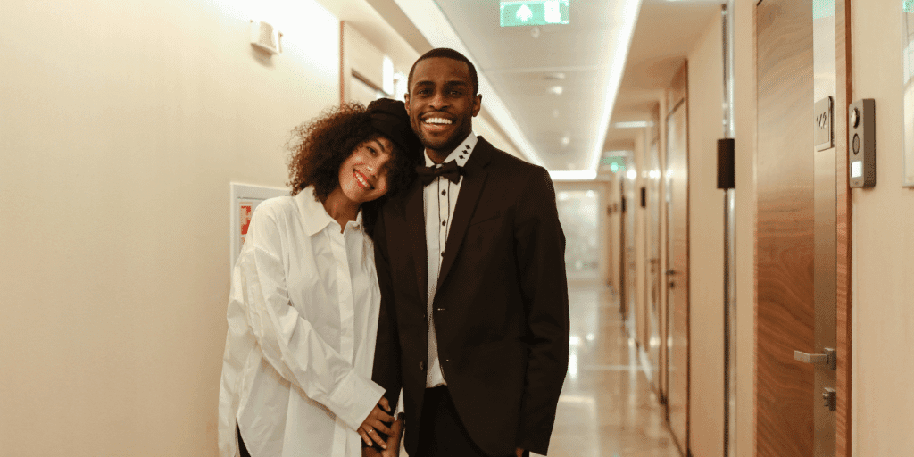 He should be reliable. An African American couple hold hands and smile while walking down a hotel hallway.