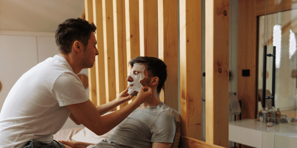 A male couple cares for each other by giving each other hydrating face masks as a gay dating tip.
