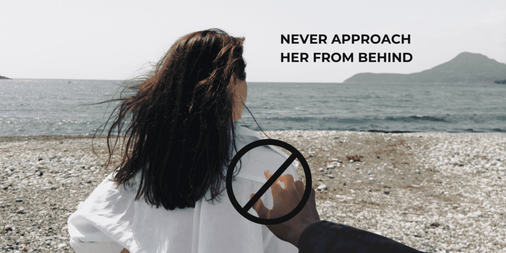 An image of the back of a woman sitting alone at the beach with the message that you should never approach her from behind to engage in conversation.