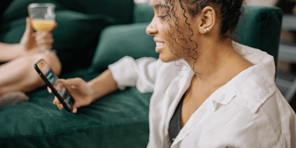Woman smiling at her phone after receiving a text message compliment from someone she met on a dating app.