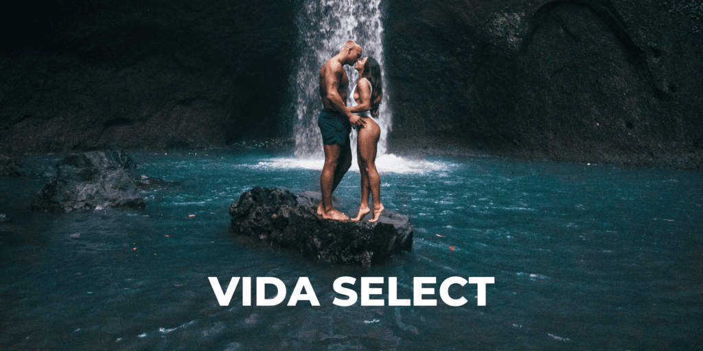 Fit couple kissing each other on rock in middle of tropical waterfall pool representing the matchmaking service Vida Select.