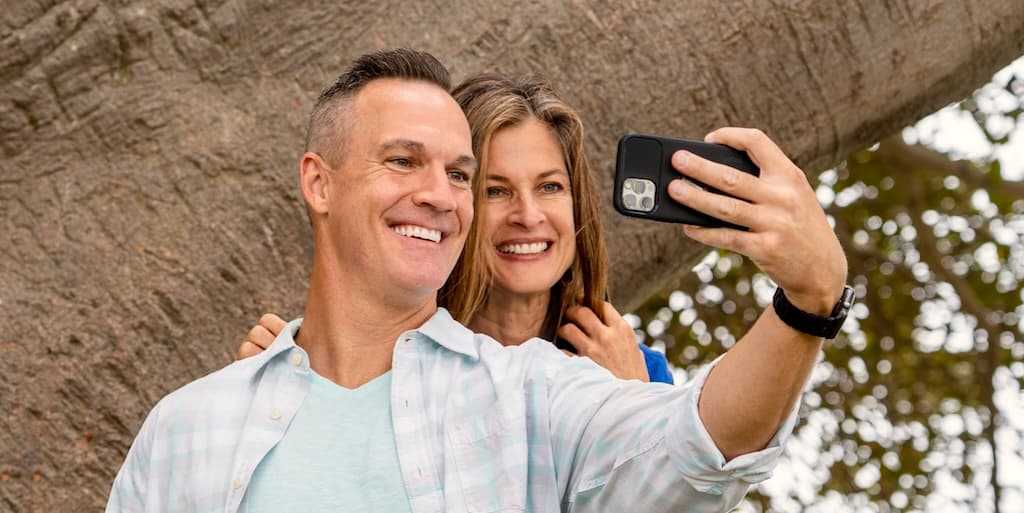 A couple in a new relationship after divorce pose with each other taking a selfie in front of a tree in a park.