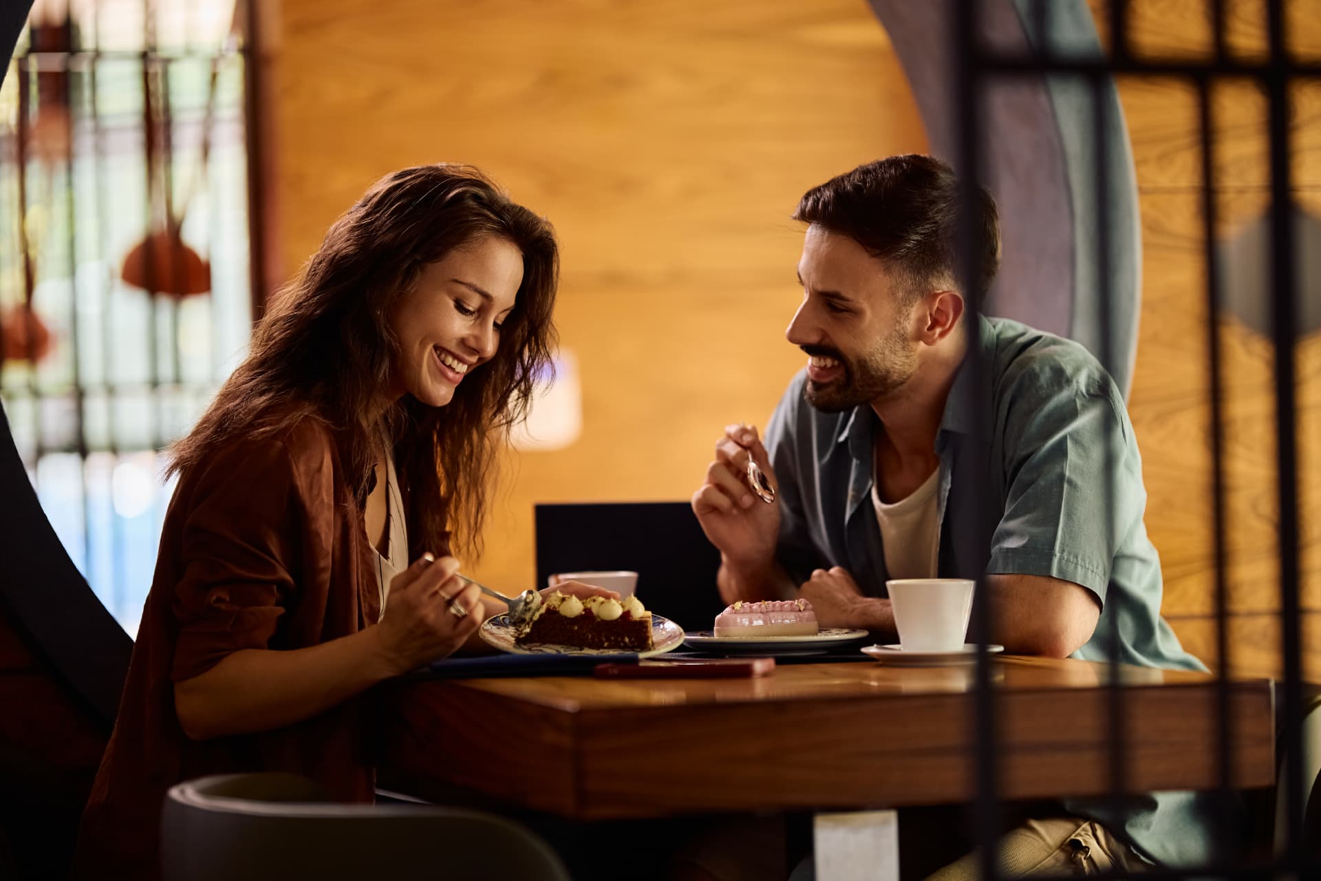 A male and female couple sit at a restaurant table enjoying dessert and coffee together.