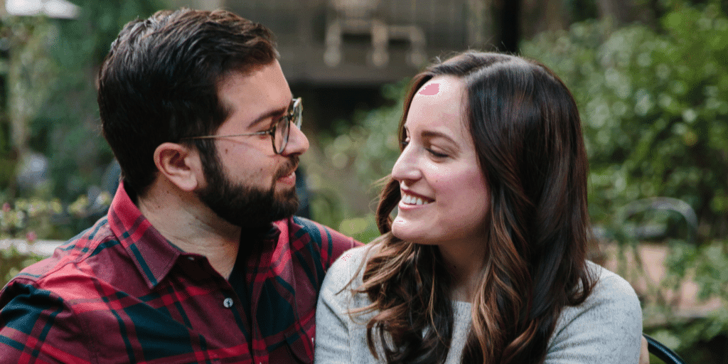 A young couple smile and laugh with each other in a park setting.