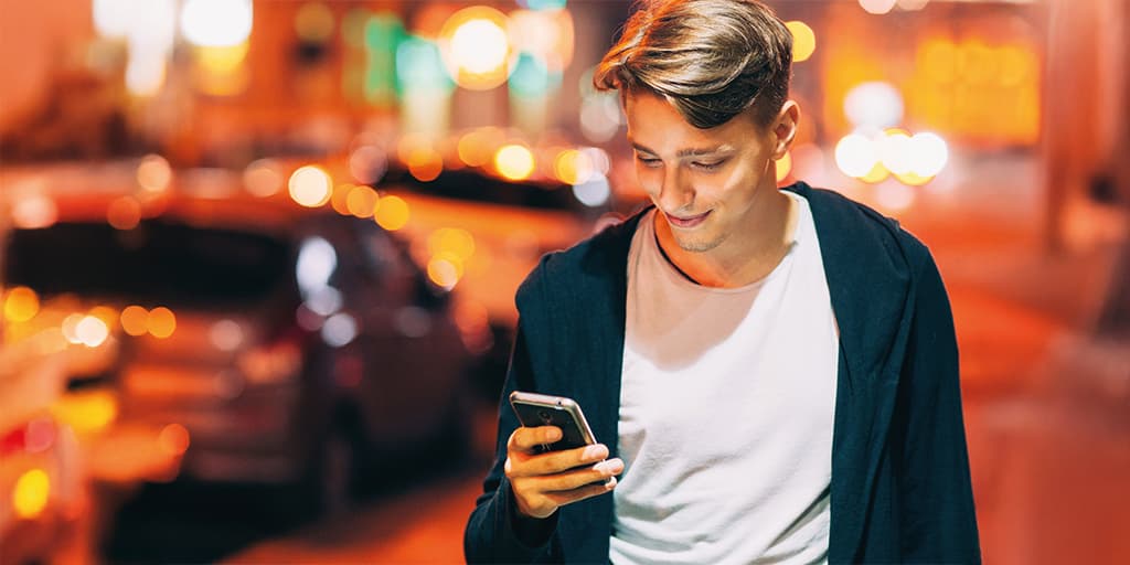 A young person walks down the street smiling at their phone feeling confident their matchmaking service is protecting their privacy while dating.