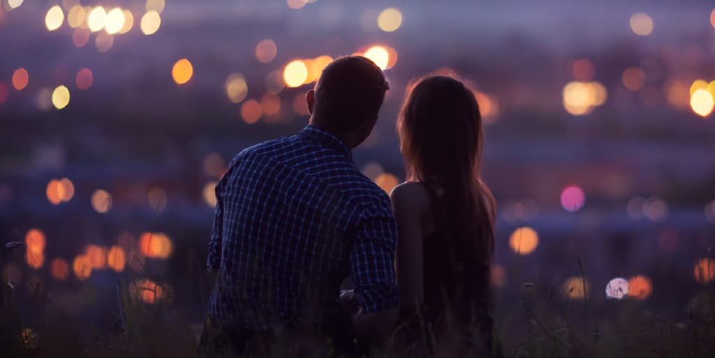A happy couple have a romantic evening viewing city lights from on top of a hill.